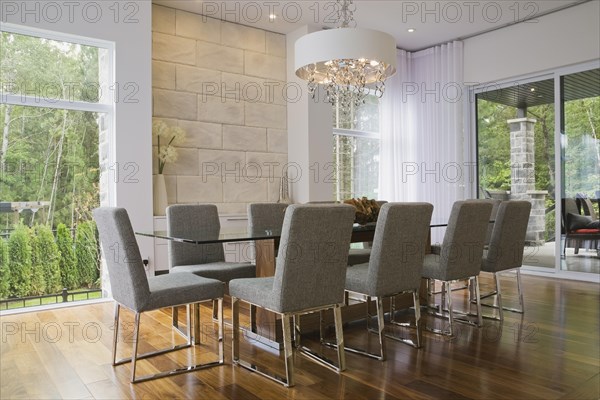 Glass dining table with gray upholstered high back chairs in dining room inside luxurious home, Quebec, Canada, North America