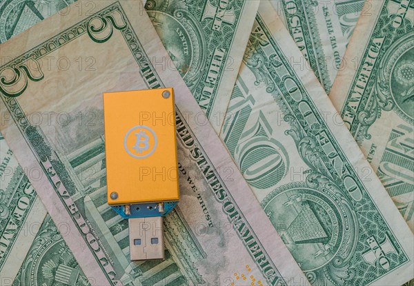 A yellow USB hardware wallet with a Bitcoin logo on a background of US dollar bills, in South Korea