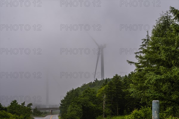 Large electric wind turbine hidden by heavy morning fog next to a two lane highway in countryside in Gangneung, South Korea, Asia