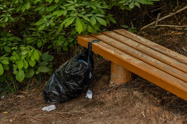 A black trash bag left beside a wooden bench in nature, in South Korea