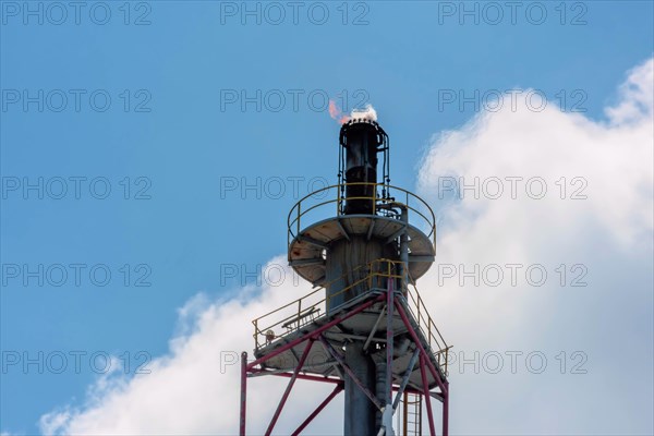 A tall flare stack emitting a flame with a blue sky in the background, in Ulsan, South Korea, Asia