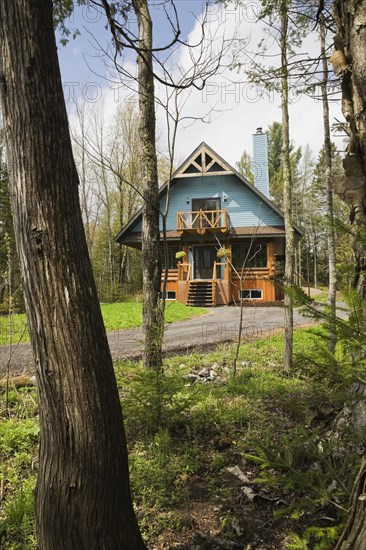 Post and beam cottage style hybrid log home facade with blue clapboard trim and timber elements in spring, Quebec, Canada, North America