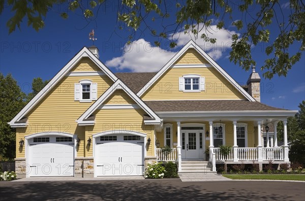 Yellow and white trim contemporary country house with two car garage, landscaped front yard and black asphalt driveway in summer, Quebec, Canada, North America