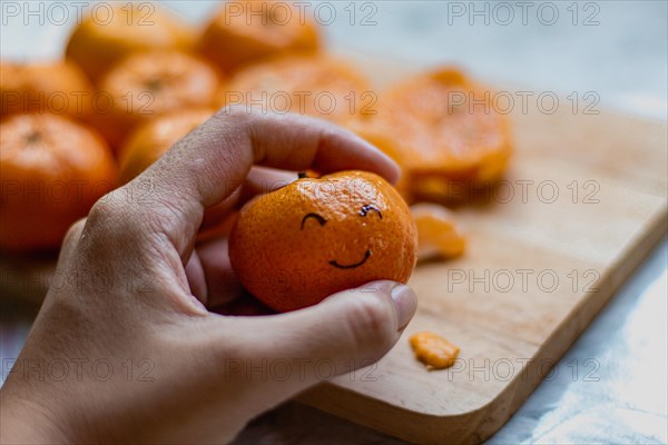 A hand holding a clementine orange fruit with a smiling face drawn on it, concept of happiness, wellness and mental health wellbeing
