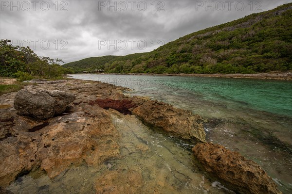 Rocky coast, long bay by the sea at sunset. Dangerous view of the Caribbean Sea. Tropical climate on a cloudy day in La Porte d'Enfer, Grande Terre, Guadeloupe, French Antilles, North America