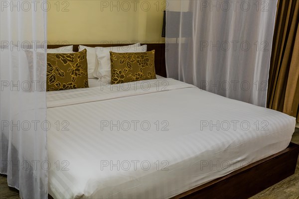 A neatly made bed with a mosquito net in a warmly lit bedroom, in Chiang Mai, Thailand, Asia