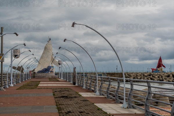 Overcast sky above a pier with arching street lamps leading towards a distant sculpture, in Ulsan, South Korea, Asia