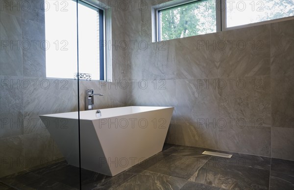 White freestanding vessel shaped bathtub in bathroom with grey ceramic tile floor and walls on ground floor inside modern cubist style home, Quebec, Canada. This image is property released. CUPR0269