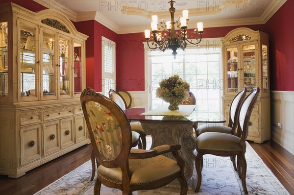 Glass top table with high-back wooden and upholstered chairs in dining room with buffets inside elegant style home, Quebec, Canada, North America