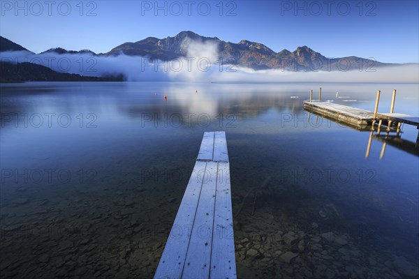 Morning atmosphere at mountain lake in front of mountains, footbridge, autumn, frost, fog, reflection, Lake Kochel, view of Herzogstand and Heimgarten, Alpine foothills, Bavaria, Germany, Europe