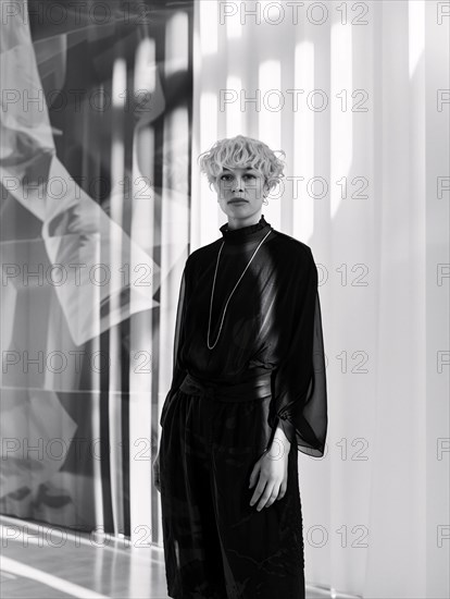 Person in stylish black outfit stands solemnly by sheer curtains, a play of light and shadow, AI generated