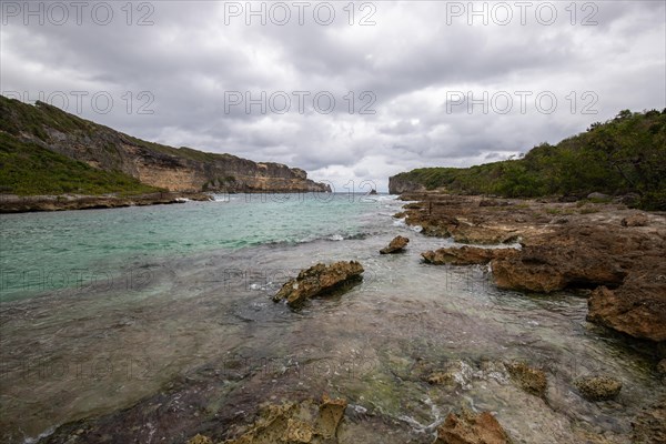 Rocky coast, long bay by the sea at sunset. Dangerous view of the Caribbean Sea. Tropical climate on a cloudy day in La Porte d'Enfer, Grande Terre, Guadeloupe, French Antilles, North America