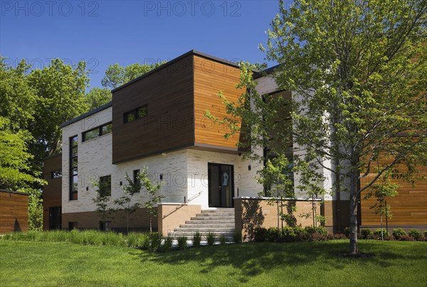 Beige stone with brown stained cedar wood modern cubist style residential home facade in spring, Quebec, Canada, North America