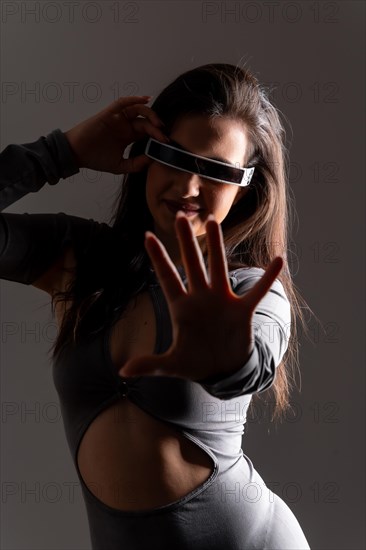 Studio portrait with grey background of a futuristic woman playing and gesturing using virtual reality mixed goggles