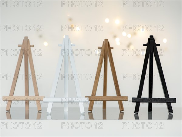 Four small wooden mini easels in the colours beech, white, bamboo and black, standing next to each other on a reflective smooth background, white background with small lights, Germany, Europe
