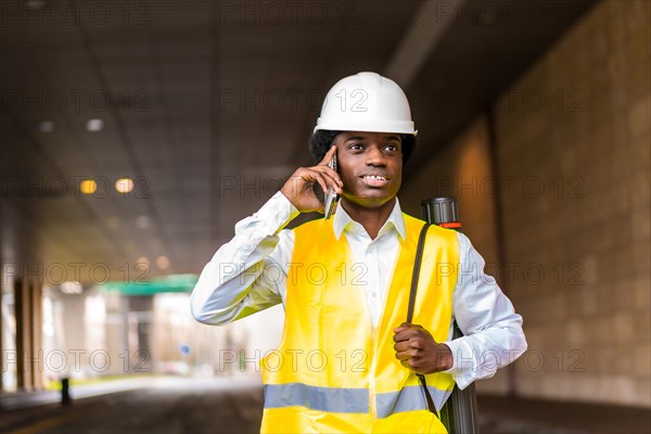 Busy young african architect using phone and walking along the city under a tunnel