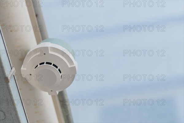 Electronic smoke detector on ceiling of enclosed pedestrian walkway with blurred plexiglass in South Korea