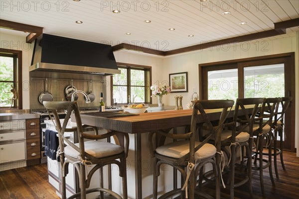 Country style kitchen with island and rustic wooden high chairs inside New Hampton style home, Quebec, Canada. This image is property released