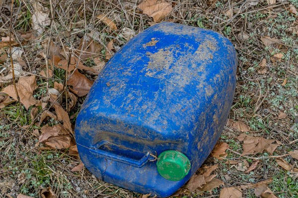 Weathered blue plastic barrel with a green cap surrounded by leaves, in South Korea