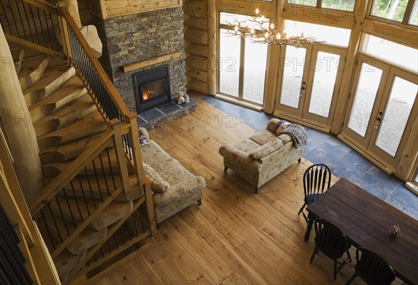 High angle view of wooden and black wrought iron staircase and living room and dining table inside handcrafted Eastern white pine Scandinavian log cabin home, Quebec, Canada, North America