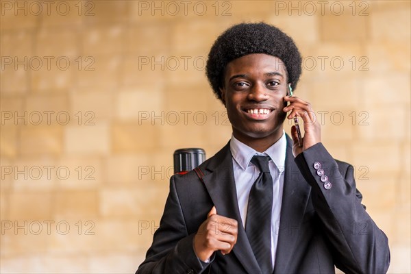 Frontal close-up portrait with copy space of a young happy architect with afro hairstyle and suit talking by phone outdoors