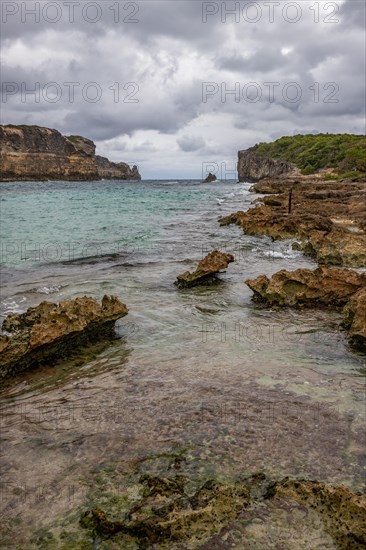 Rocky coast, long bay by the sea at sunset. Dangerous view of the Caribbean Sea. Tropical climate on a cloudy day in La Porte d'Enfer, Grande Terre, Guadeloupe, French Antilles, North America