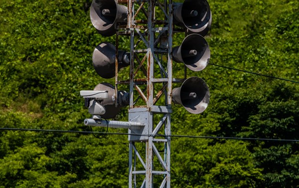 Communication tower consisting of loud speakers, solar panel and closed circuit camera with tree covered mountain in background in South Korea