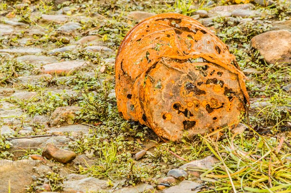 A rusty, decayed bucket lies on a grassy cobblestone surface, showing signs of erosion, in South Korea
