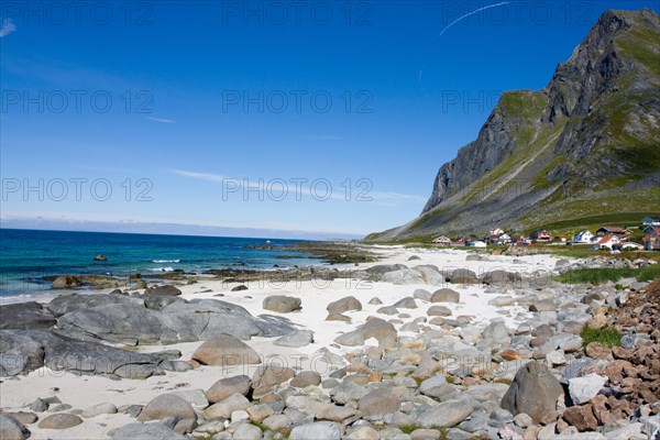 An idyllic sandy beach with rocks and clear water against a backdrop of mountains and blue skies Vikten Lofoten