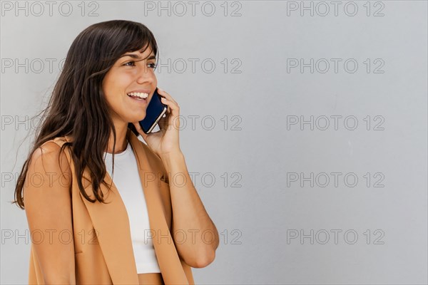 A woman is talking on her cell phone while wearing a tan jacket. She is smiling and she is in a good mood