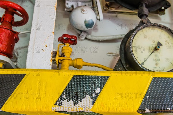 Old pressure gauge mounted above yellow and black striped ledge with valves and bell in background in Gangneung, South Korea, Asia