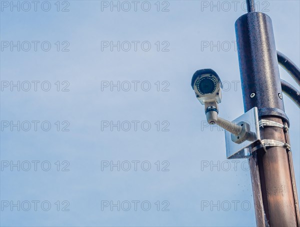Surveillance camera mounted on metal light pole with blue sky and puffy white clouds in background in South Korea