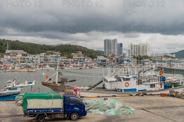 Fishing boats docked in a harbor with a truck and nets in the foreground, under an overcast sky, in Ulsan, South Korea, Asia