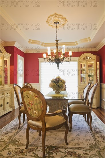 Glass top table with high-back wooden and upholstered chairs in dining room with buffets inside elegant style home, Quebec, Canada, North America