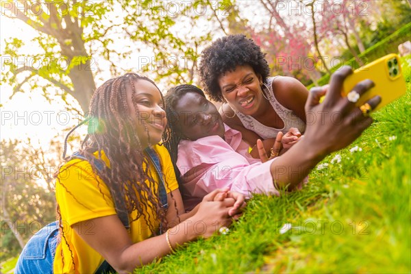 African american female young friends taking selfie lying together in a park
