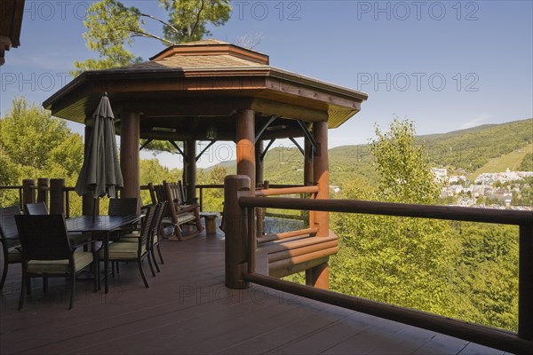 Brown stained gazebo on wooden deck with tempered glass and log railings attached to back of luxurious log cabin home overlooking Mt-Tremblant ski resort in summer, Quebec, Canada, North America
