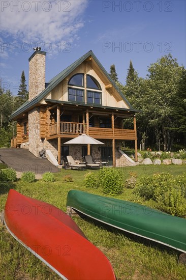 Handcrafted two story spruce log home cabin with fieldstone chimney, green sheet metal roof and red and green canoes in summer, Quebec, Canada, North America