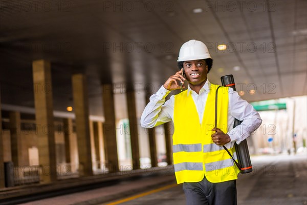 Young african architect talking to the mobile while walking quick outdoors