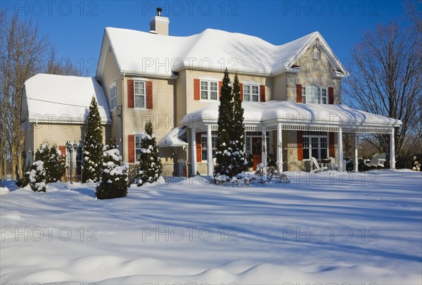 Two story beige vinyl siding with brownish red nuanced brick veneer and orange trim home in winter, Quebec, Canada, North America