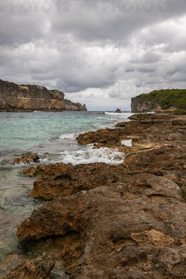 Rocky coast, long bay by the sea at sunset. Dangerous view of the Caribbean Sea. Tropical climate on a cloudy day in La Porte d'Enfer, Grande Terre, Guadeloupe, French Antilles, North America