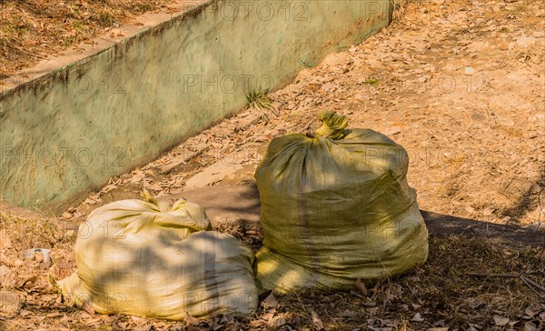 Two tied green garbage bags on a concrete path beside dirt, in South Korea