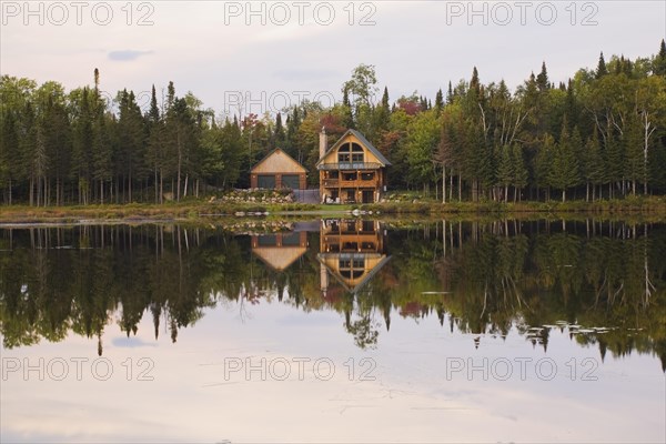 Garage and handcrafted two story spruce log cabin home with fieldstone chimney and green sheet metal roof on edge of lake in autumn, Quebec, Canada, North America