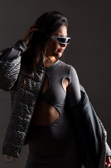 Vertical studio portrait with grey background of a futuristic woman in fashion clothes wearing intelligent goggles