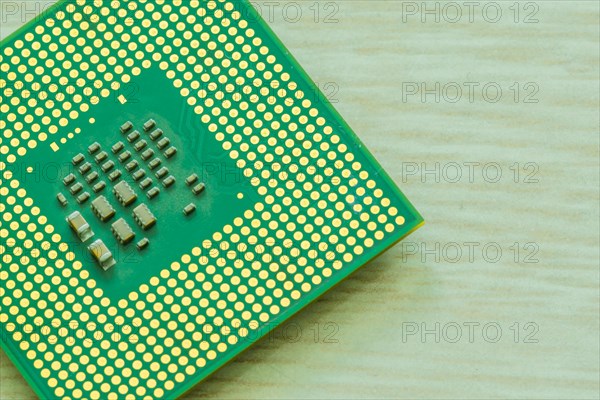 Bottom side of central processor unit (CPU) detailing the individual chips and gold connection pins on blurred wood grain table top