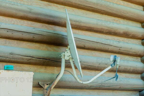 Satellite television receiver dish mounted on exterior wall of log cabin in South Korea