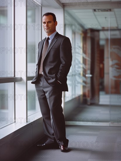 Businessman in suit and tie standing thoughtfully by a window in a modern office environment, AI generated