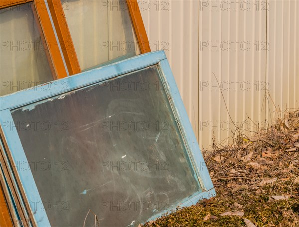 Leaning discarded window frames against a metal siding near weeds, in South Korea