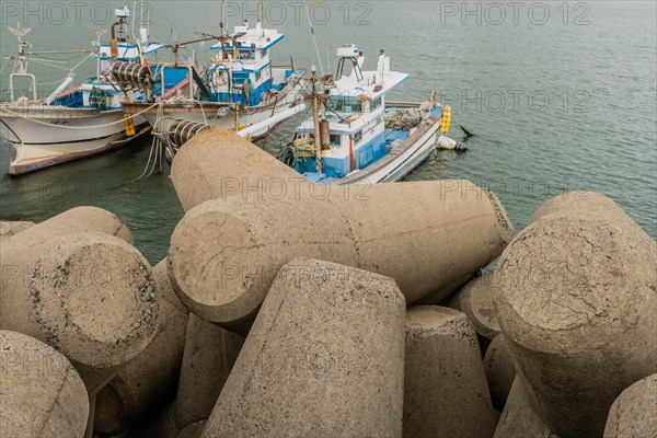 Fishing boats docked at a marina, surrounded by concrete wave blocks on a cloudy day, in Ulsan, South Korea, Asia