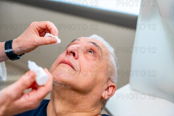 Ophthalmologist applies drops to dilate the pupil to a man before a glaucoma test on the eye with a laser machine