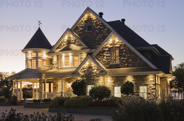 Elegant grey stone with white trim and blue asphalt shingles roof Victorian home facade at dusk in summer, Quebec, Canada, North America